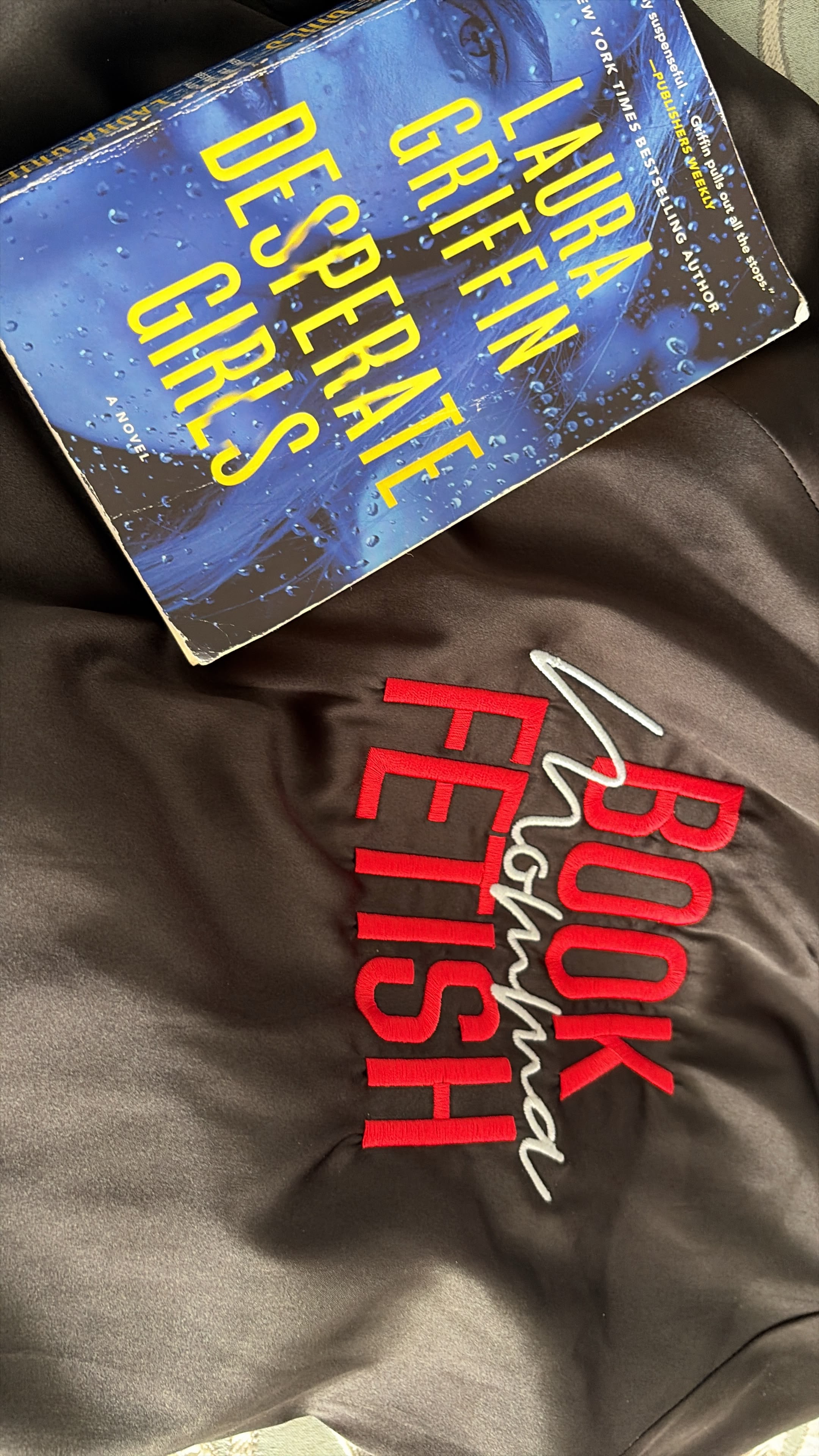A close-up of the Book Fetish Momma bomber jacket embroidery next to July’s pick, Desperate Girls