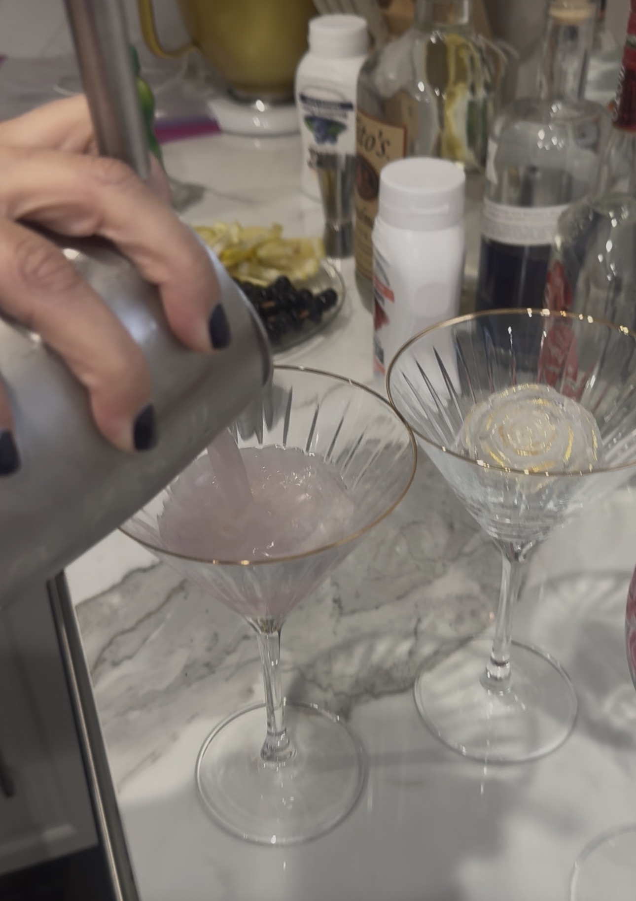 A lychee martini being poured from a shaker into a gold-rimmed martini glass
