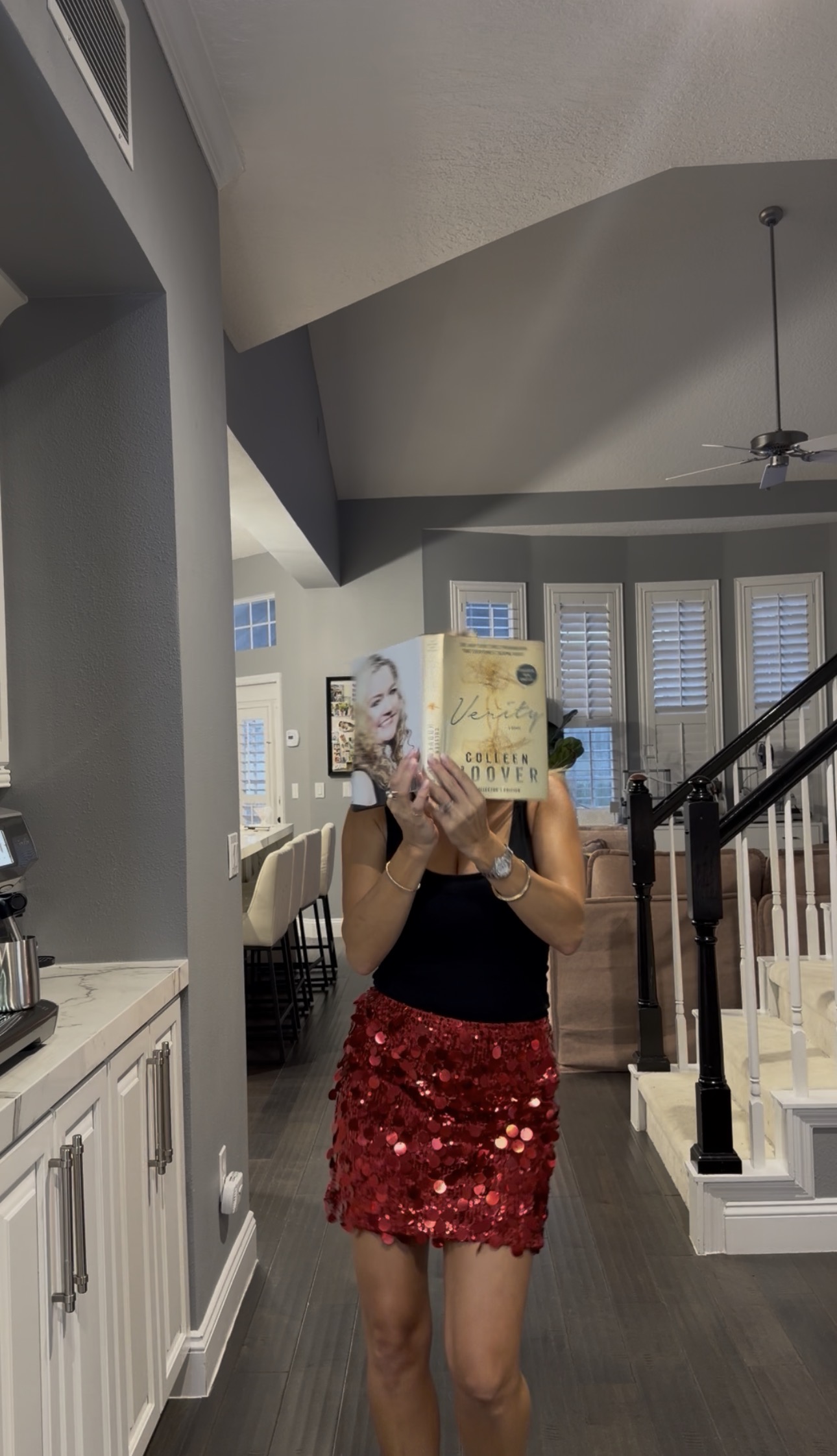 A Book Fetish Momma in a red sequin skirt holding a copy of Verity by Colleen Hoover in front of her face